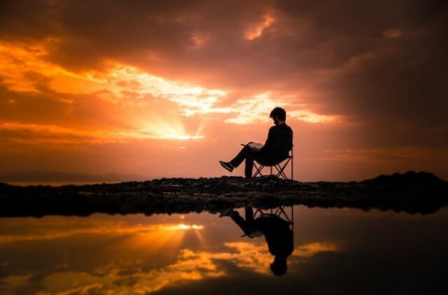 Homme lisant un livre sur une chaise à l'extérieur pendant le coucher du soleil