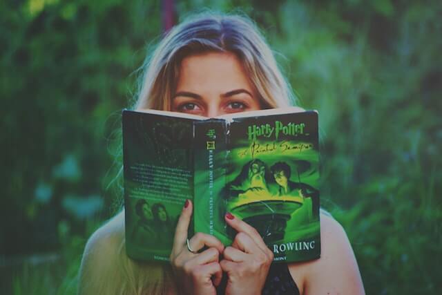 Une fille qui cache son visage derrière un livre d'Harry Potter en ne montrant que les yeux