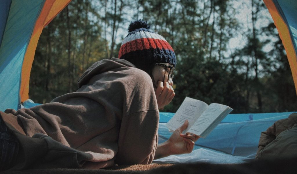 Une personne à l'intérieur d'une tente, plongée dans un livre, trouvant le réconfort et la détente dans la lecture au milieu de la nature.